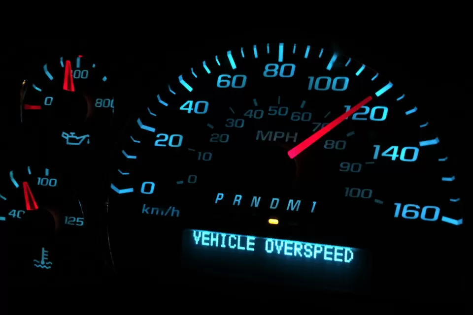 Close-up of car speedometer showing 120 mph speed with digitally displayed ' VEHICLE OVERSPEED' warning